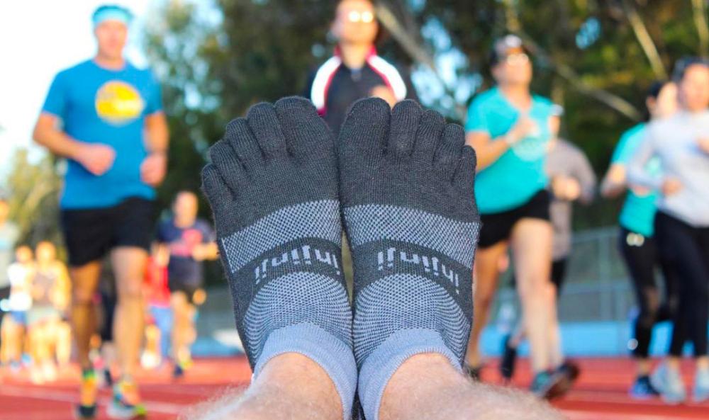 Closeup of someone's feet wearing the Injinji Trail Midweight Mini-Crew in Granite, with track runners running in the background. 