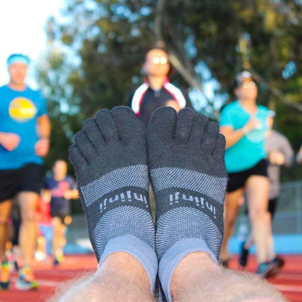 Closeup of someone's feet wearing the Injinji Trail Midweight Mini-Crew in Granite, with track runners running in the background. 