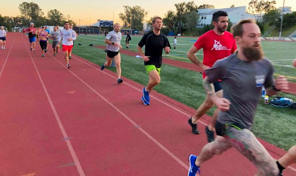 Several people running on a track in the early evening.