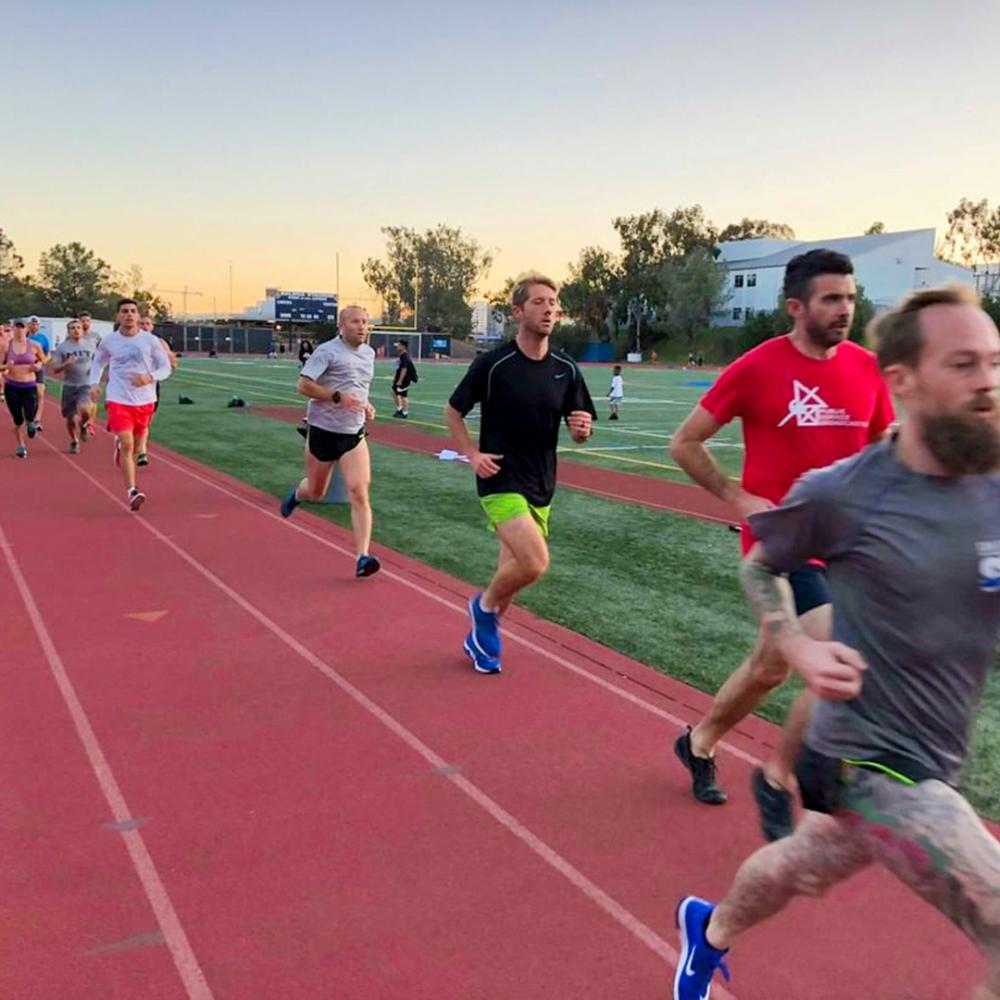 Several people running on a track in the early evening.