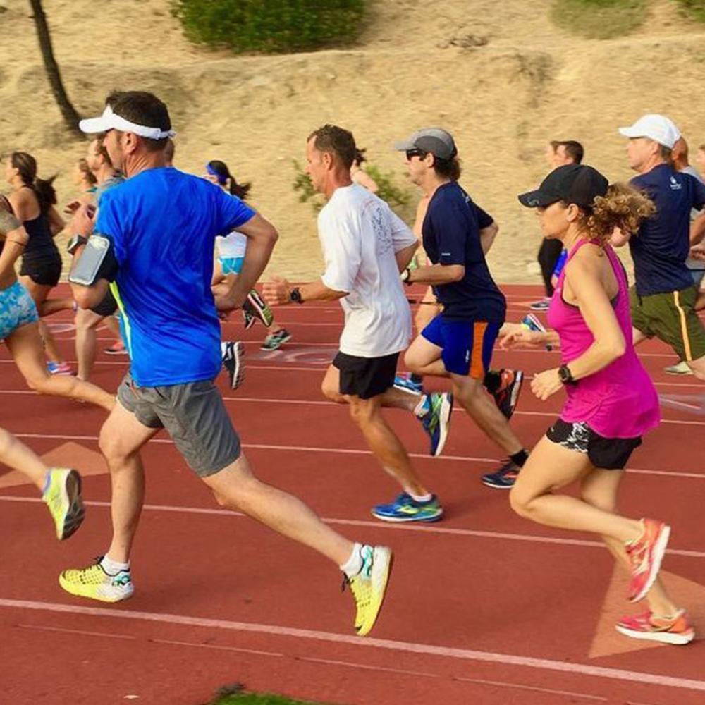 A group of 15 people in full stride running on a track.