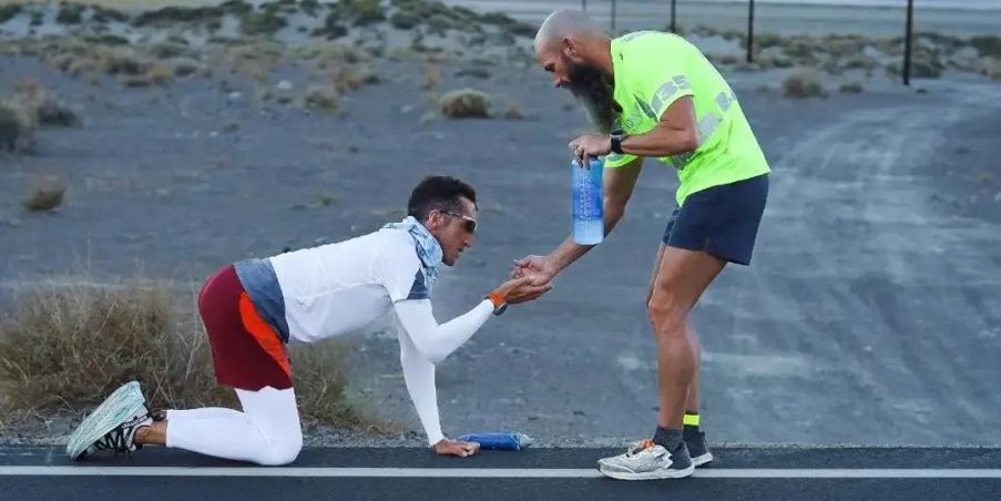 Mike McKnight crawling on the ground at Badwater 135 with Ben Light reaching down to assist him. 