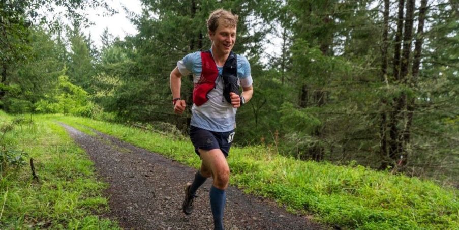 Team Injinji Athlete Andrew Miller running on a lush forested trail.