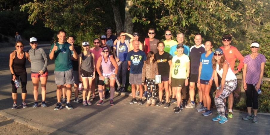 A group of twenty or more men and women posing together in an asphalt lot. 