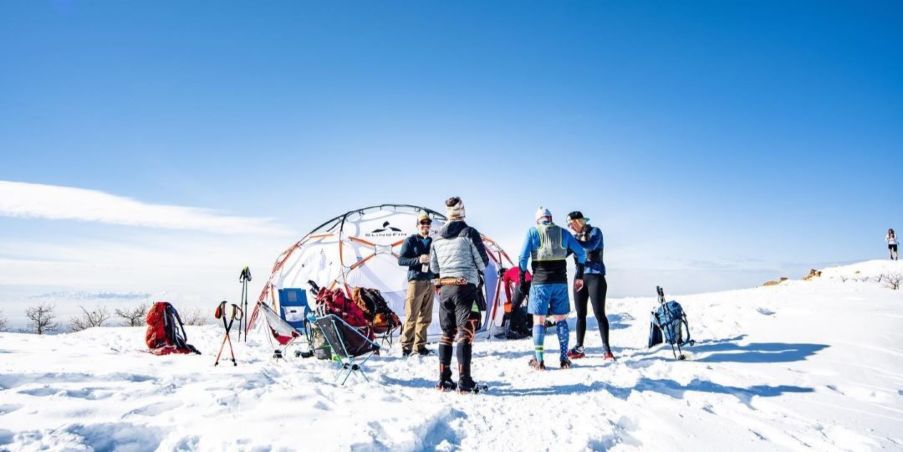 A group of people wearing running gear while standing around a dome in the middle of a vast snowy area.