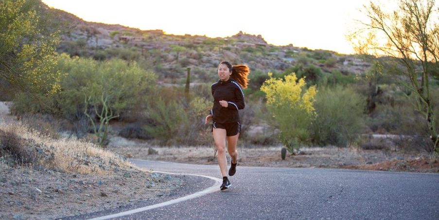 An young woman running on a curved desert road in the late afternoon. 