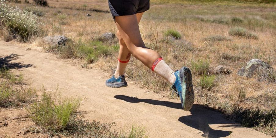 Female running on a dirt trail wearing blue running shoes and black running shorts. 