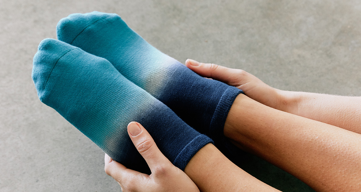 Woman sitting on the ground stretching wearing Injinji X Pointe Studio Grip Full Foot No-Show socks in Teal Crush 