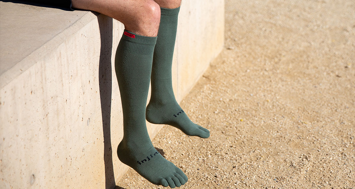 A man sitting with his legs dangling over the edge wearing over the calf Injinji socks.