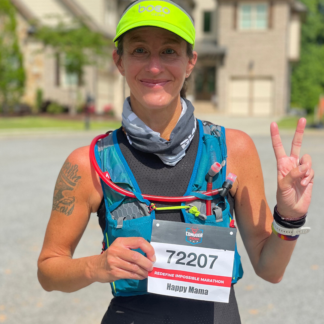 Karin Bachrodt wearing running gear, holding up her race bib, and making a peace sign.