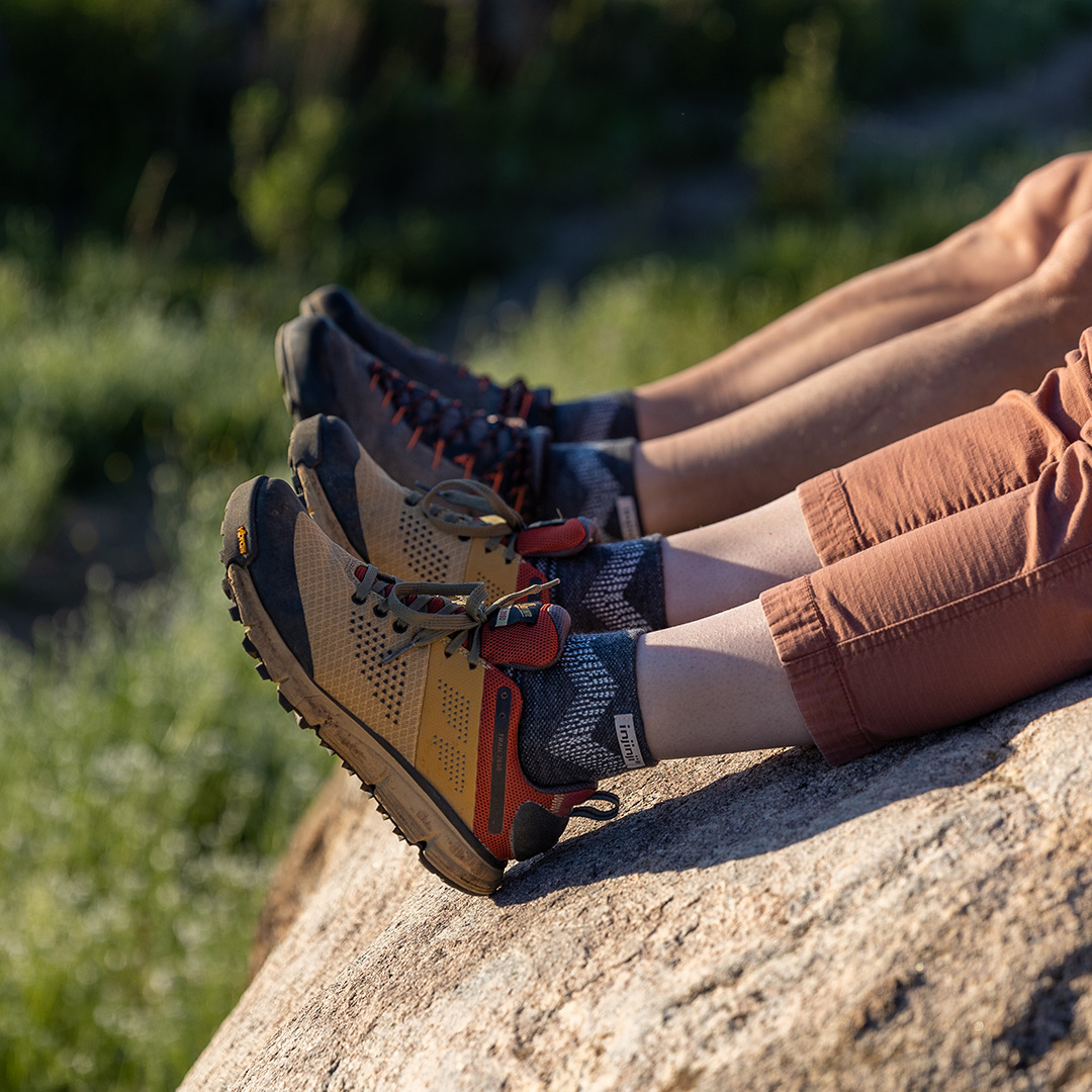 Two hikers taking a break on a large boulder wearing the Injinji Outdoor Midweight Mini-Crew wool socks. 