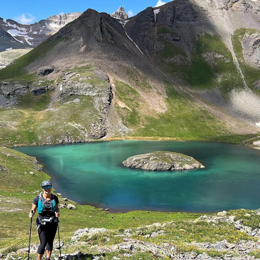 Team Injinji athlete Angela Shartel posing in front of an alpine lake at Hardrock 100 ultramarathon.