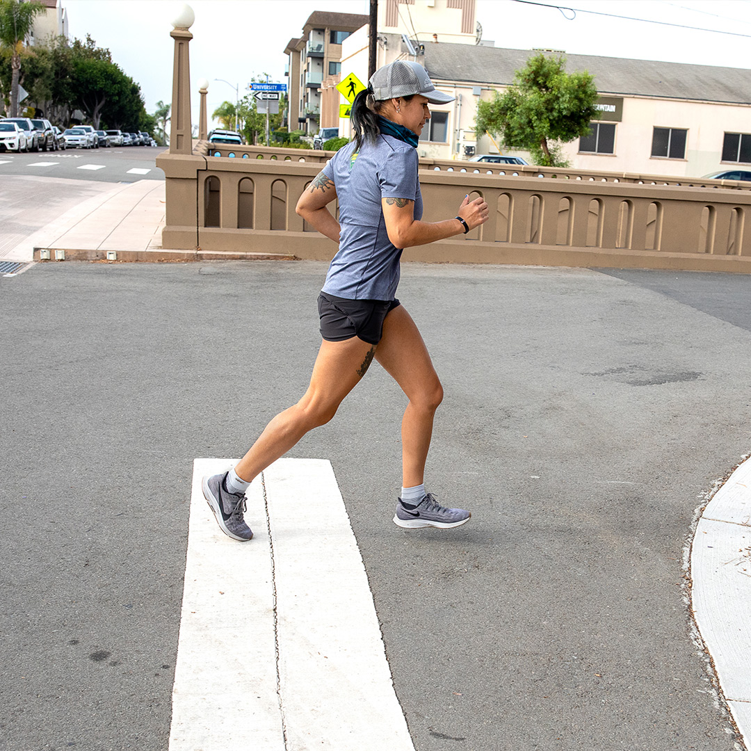 A woman wearing running apparel and Injinji running performance socks, jogging through a pedestrian crosswalk.