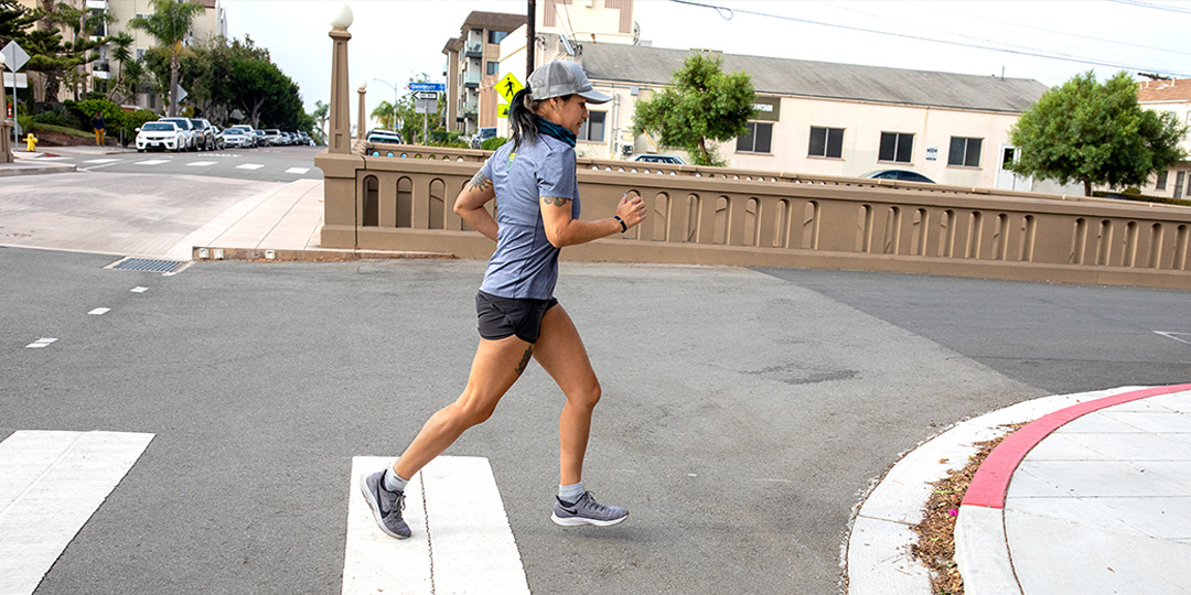 A woman wearing running apparel and Injinji running performance socks, jogging through a pedestrian crosswalk.