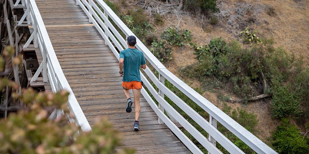 A man wearing running apparel, jogging over a wooden bridge. 