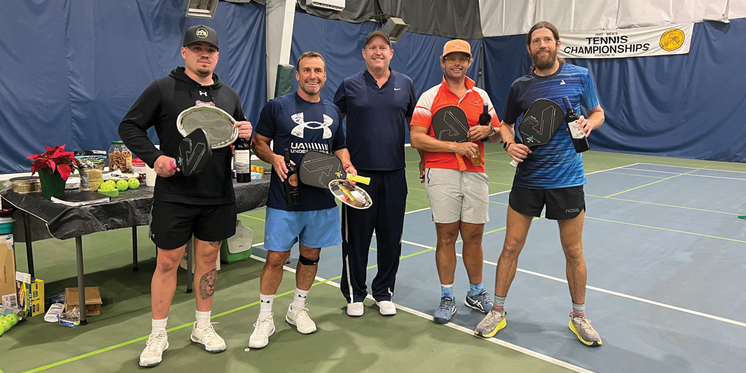 Mike Wardian posing with fellow pickleball players inside an indoor pickleball court. 