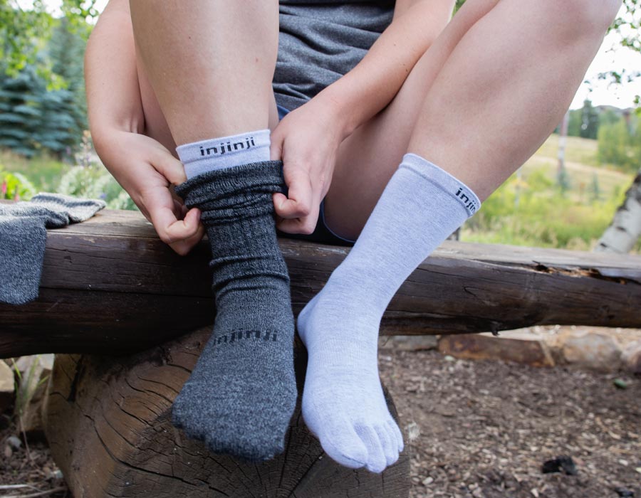 A hiker sitting on a log adjusting the Liner Crew baselayer and Hiker Crew top sock. 