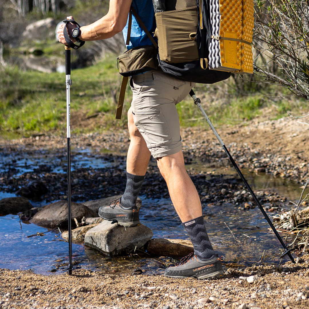 A hiker wearing the Outdoor Midweight Crew Wool socks crossing a stream with hiking poles. 