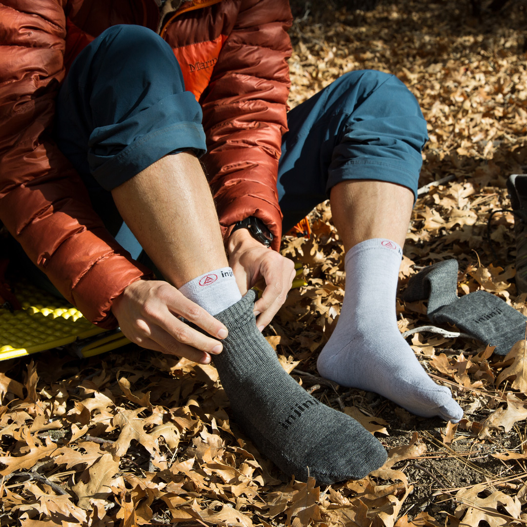 A hiker sitting on leaf covered ground, adjusting the Liner Crew baselayer and Hiker Crew topsock. 