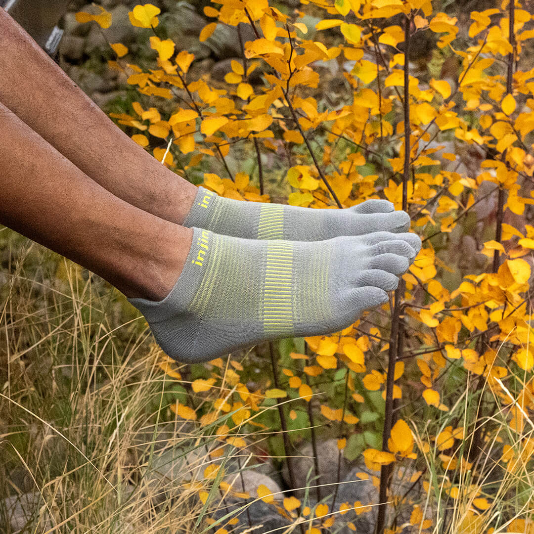 A runner bending down to adjust their Injinji Run Lightweight Mini-Crew running socks. 