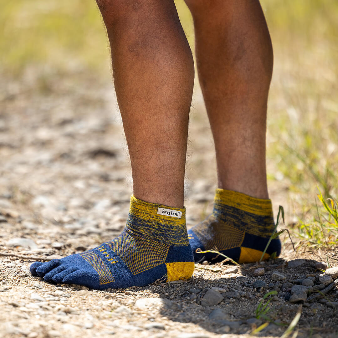 Runner sitting on a rock adjusting his Trail Midweight Mini-Crew toesocks. 