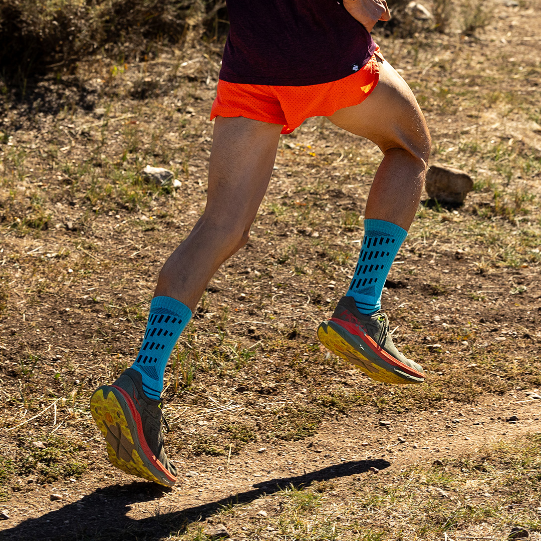 A man in full stride running on pavement in a residential area wearing the Injinji Ultra Run Crew running socks in Obsidian. 