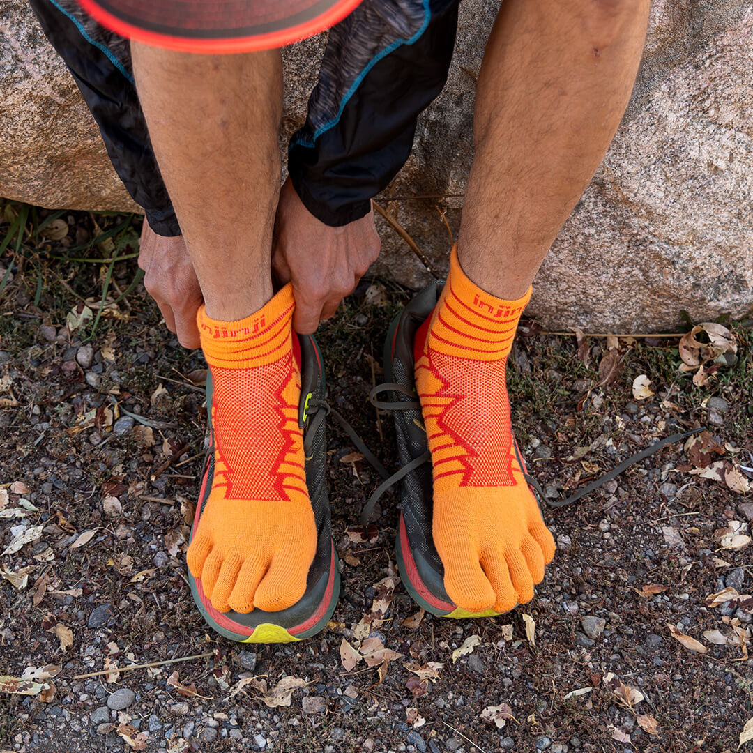 A man standing on a dirt trail turned away from the camera, wearing the Injinji Ultra Run Crew running socks in Cobalt. 